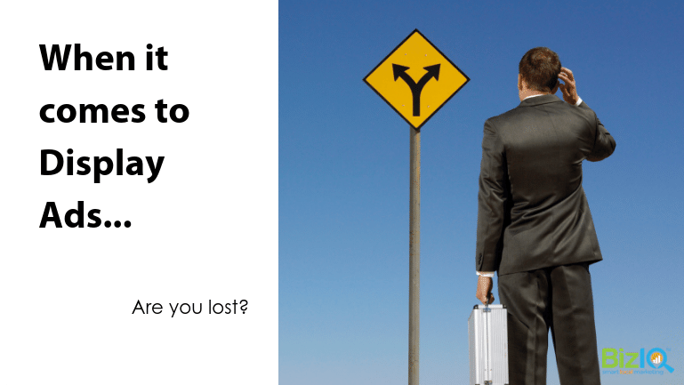 Image: A man in a suit, holding a silver case, scratches his head in front of a yellow road sign with 2 diverging arrows pointed upwards in opposite directions. Text reads When it comes to Display Ads...Are you lost?