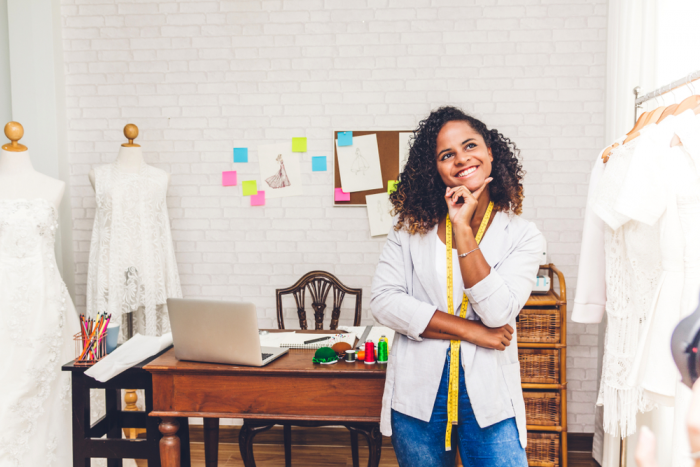 african american woman business owner in white jacket in her office surrounded by dresses, looking up to think about video for YouTube